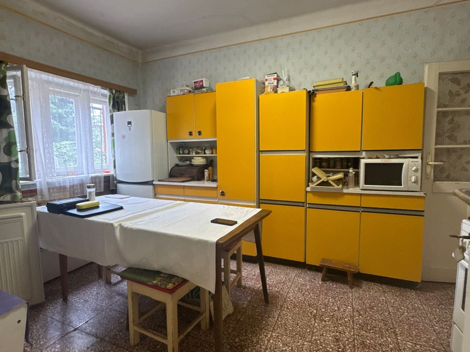 Konyha sárga szekrénysorral, étkezőasztallal és két ablakkal